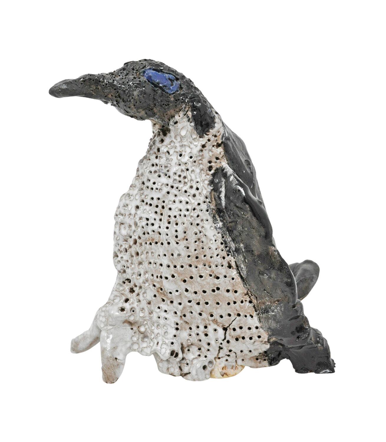 a small ceramic sculpture of a penguin. It is shown in profile, facing toward the left, and is glazed to have a blue eye, white stomach, and black head and back. The artist has textured the penguin's stomach with stippled holes.