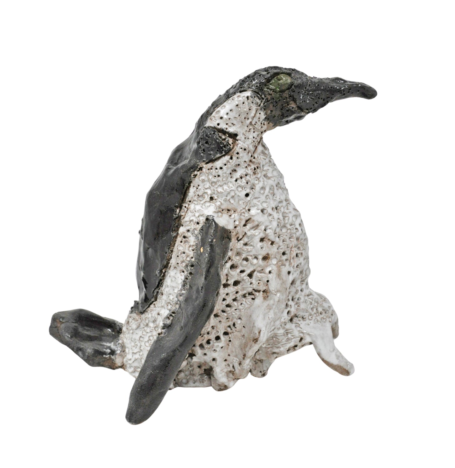 another angle of the small ceramic sculpture of a penguin. It is shown in profile, facing toward the right, and is glazed to have a blue eye, white stomach, and black head and back. The artist has textured the penguin's stomach with stippled holes.