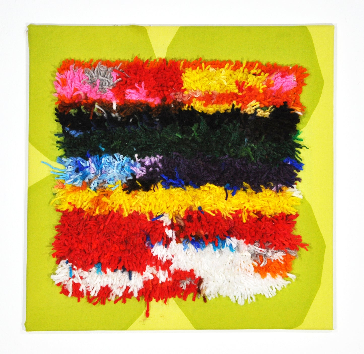 a tufted yarn fiber work adhered to a piece of green and yellow fabric. The fabric has been stretched over stretcher bars so that it can hang on the wall. The pattern on the tufted square is horizontal stripes made from red, green, yellow, and white pieces of yarn. 